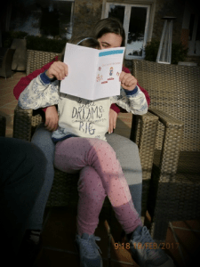 Fotografia d’una nena asseguda llegint el llibre Dibuixa’t el teu llibre