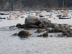Costa de Calella amb roques en primer pla i barques ancorades al fons