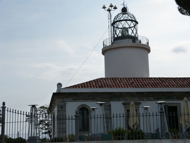Fotografia del Far de Sant Sebastià amb torre cilíndrica blanca, galeria i edifici annex amb arcs