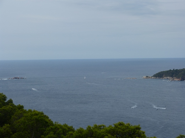 Vista des del Far de Sant Sebastià amb mar en calma, barques i línia costanera arbrada