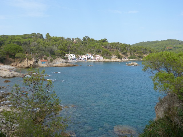 Vista costanera amb edificis blancs entre arbres, aigües clares i cel serè