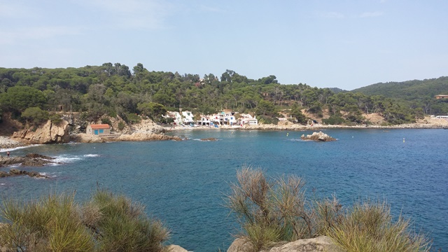 Vista des d’un mirador costaner amb roques, mar blau, vegetació i edificis blancs al fons