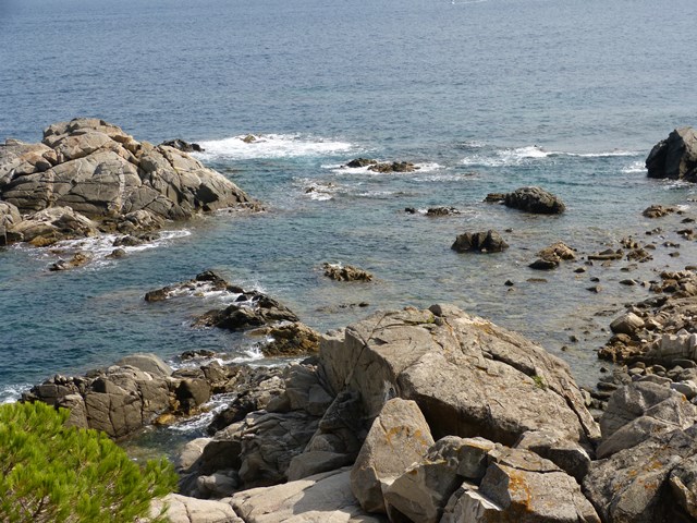 Vista costanera amb onades trencant contra roques, textura marina i pedres en primer pla