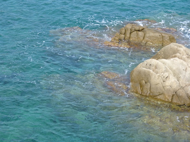 Vista costanera amb roques clares submergides, aigües blaves i verds intensos