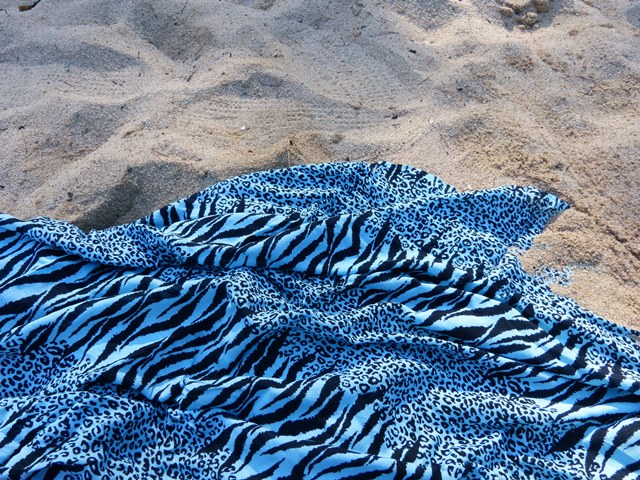 Fotografia d’un teixit amb estampat de zebra blau i negre sobre sorra de platja