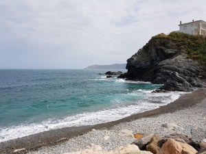 Platja rocosa de Llançà amb onatge i edifici sobre penya-segat