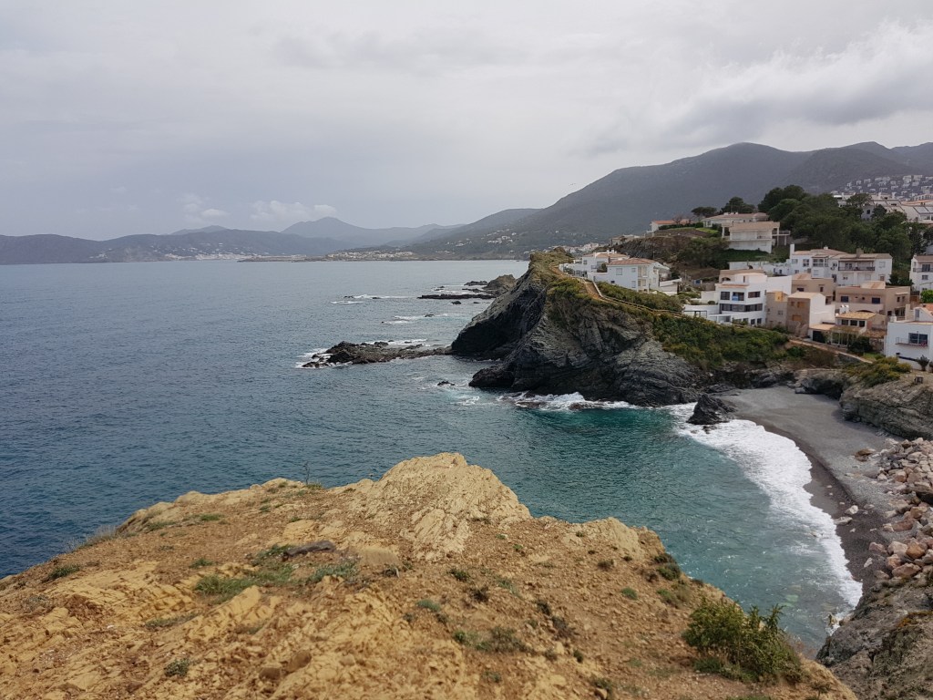 Vista panoràmica de Llançà amb costa rocosa, edificis i muntanyes al fons