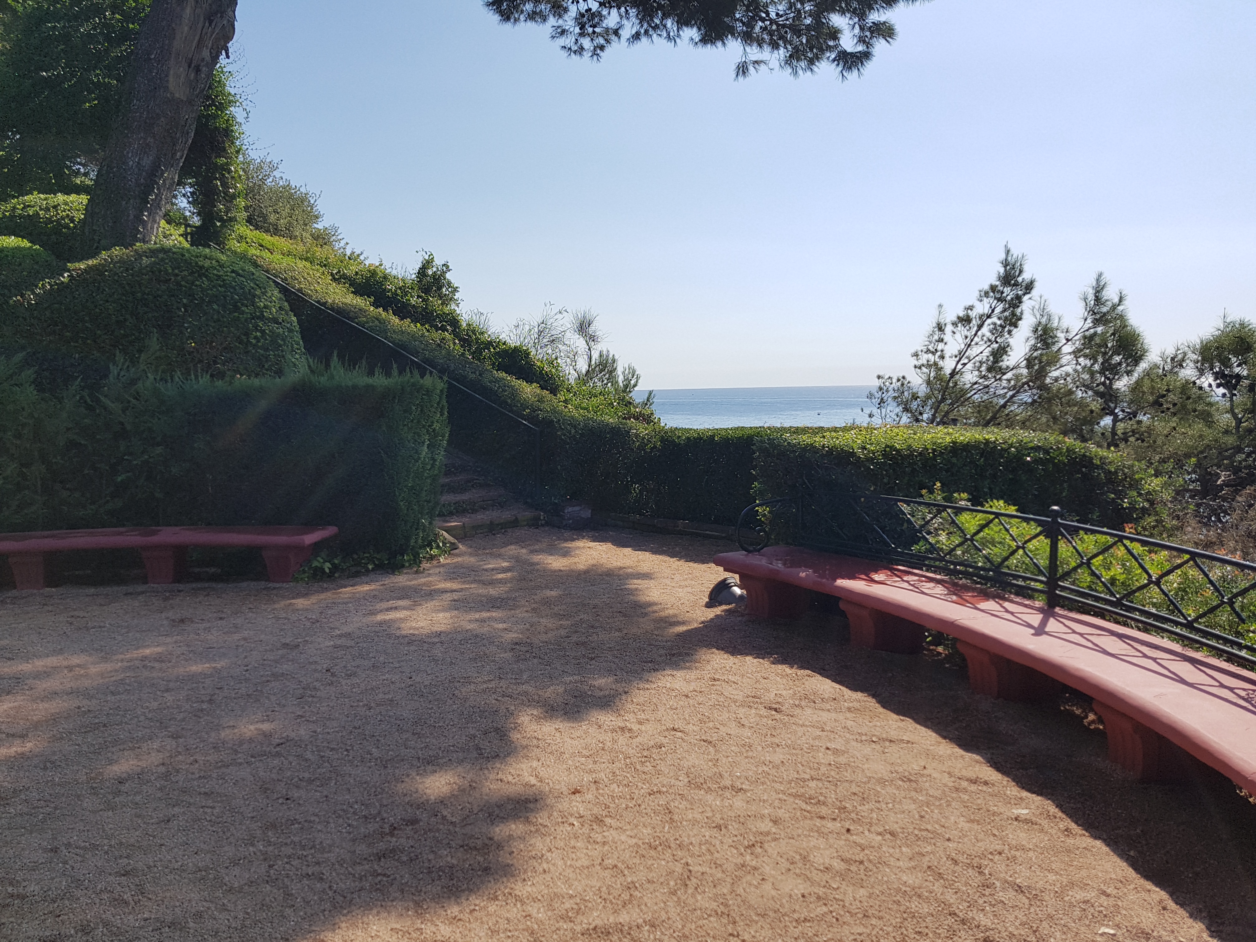 Banc corbat entre arbustos i arbres amb vista al mar als Jardins de Santa Clotilde