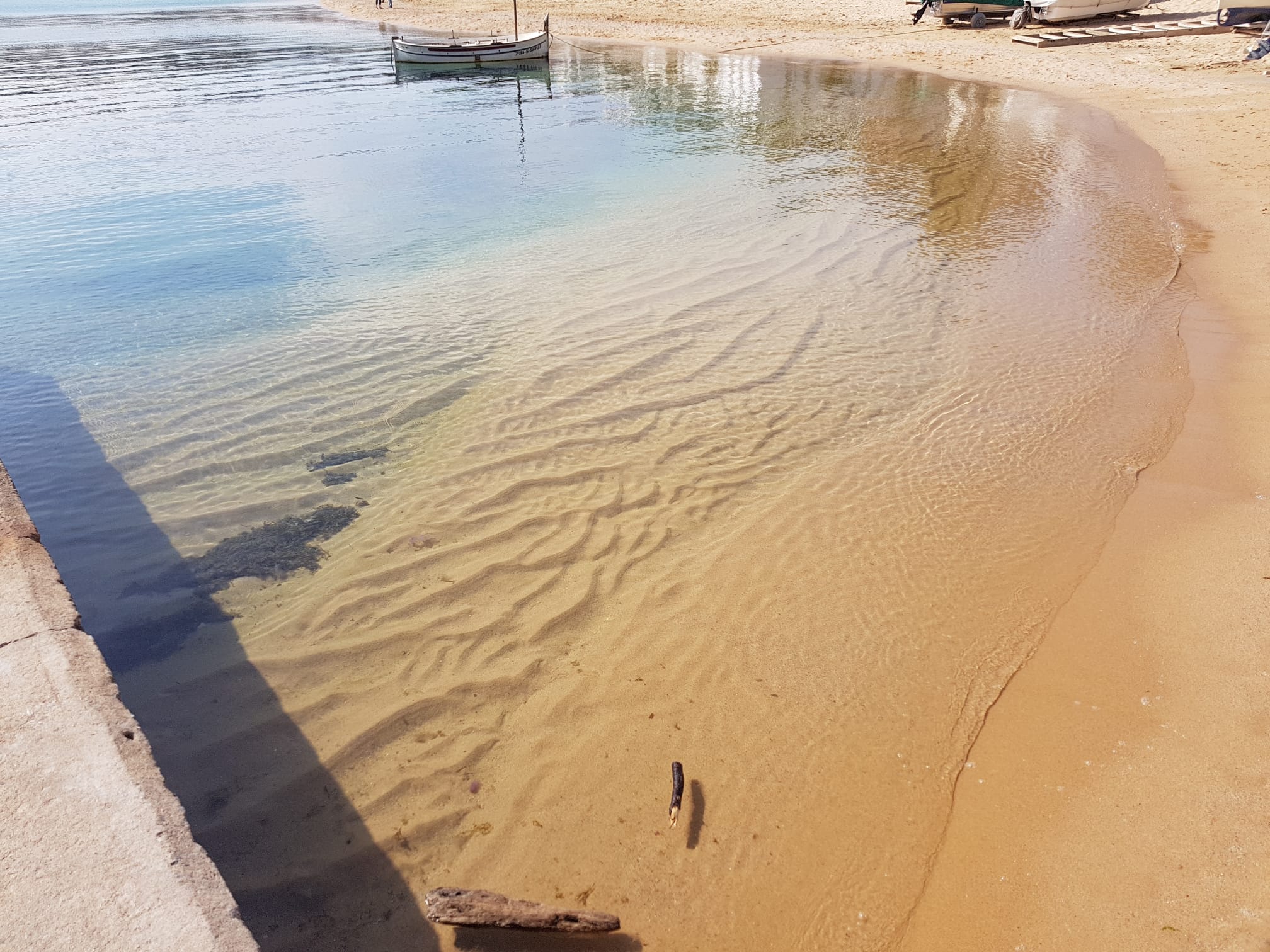 Platja amb onades suaus, sorra clara i reflexos d’edificis a Calella de Palafrugell