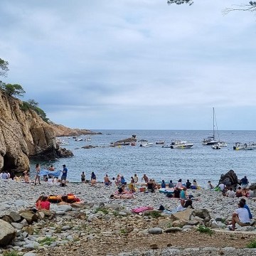 Cala Pedrosa amb roques, barques i persones prenent el sol