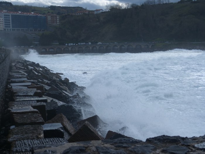 Onades trencant amb boira i edificis al fons sota cel gris al Mar Cantàbric