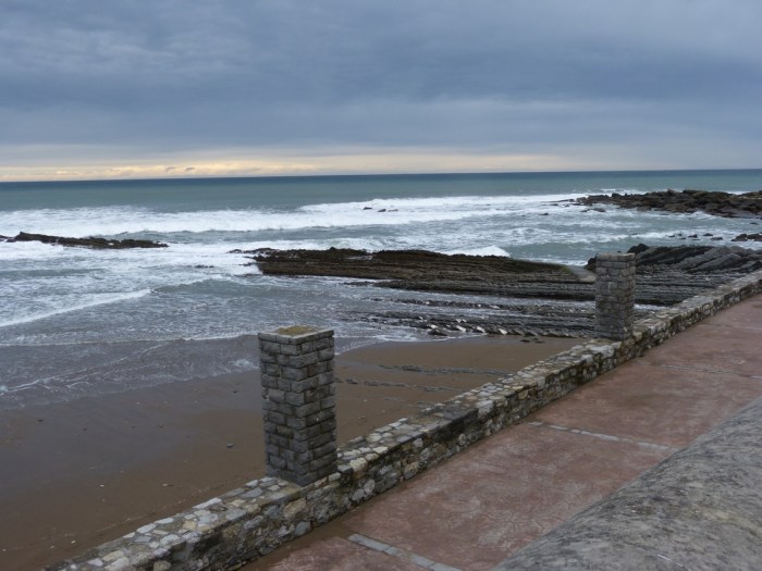 Passeig pavimentat amb barana de pedra davant del mar Cantàbric i cel ennuvolat