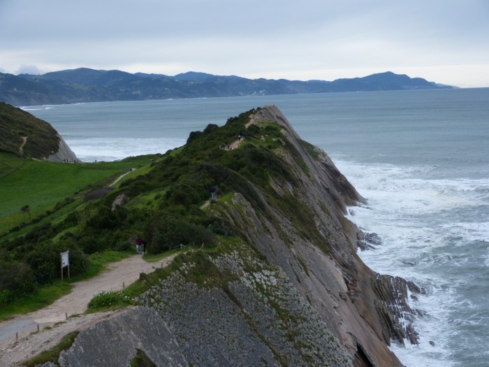 Camí estret sobre penya-segat amb figura solitària i mar Cantàbric al fons