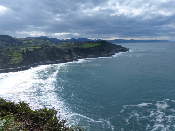 Vista de penya-segats verds amb mar Cantàbric i horitzó muntanyós sota cel gris