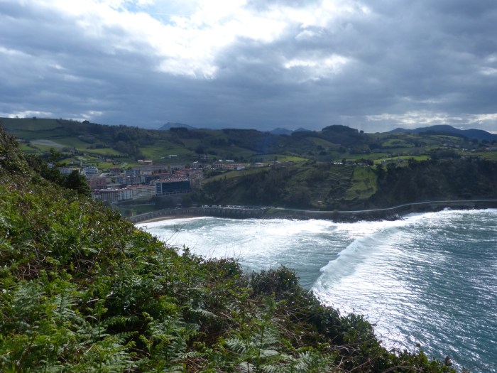 Vila costanera entre penya-segats verds amb mar Cantàbric i cel dramàtic