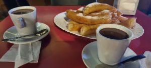 Dues tasses de xocolata calenta amb xurros en safata vermella