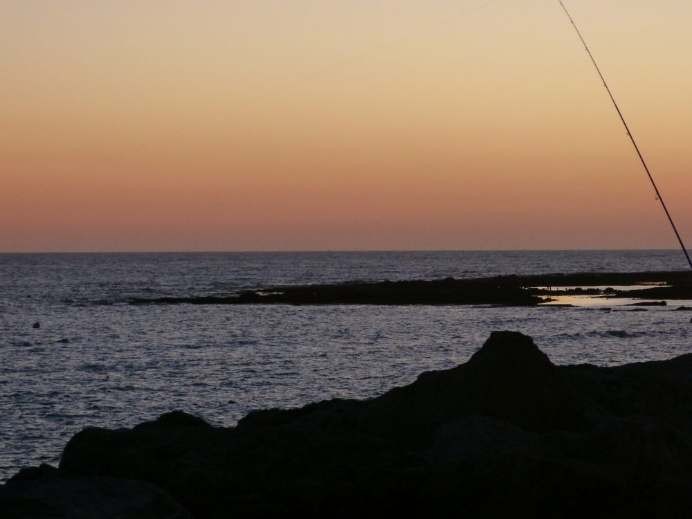 Canya de pescar sobre roques amb cel taronja i violeta al capvespre a Puerto Sherry