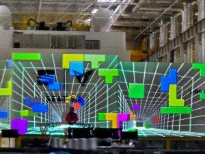 Figura humana davant d’una animació digital en espai industrial amb quadrícules flotants