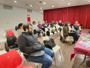 Públic assegut en sala amb cortines vermelles durant presentació literària