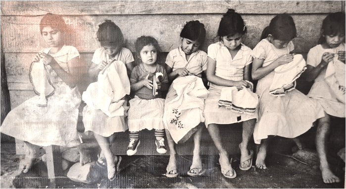 Fotografia en blanc i negre que mostra dues nenes immerses en una activitat de brodat. 