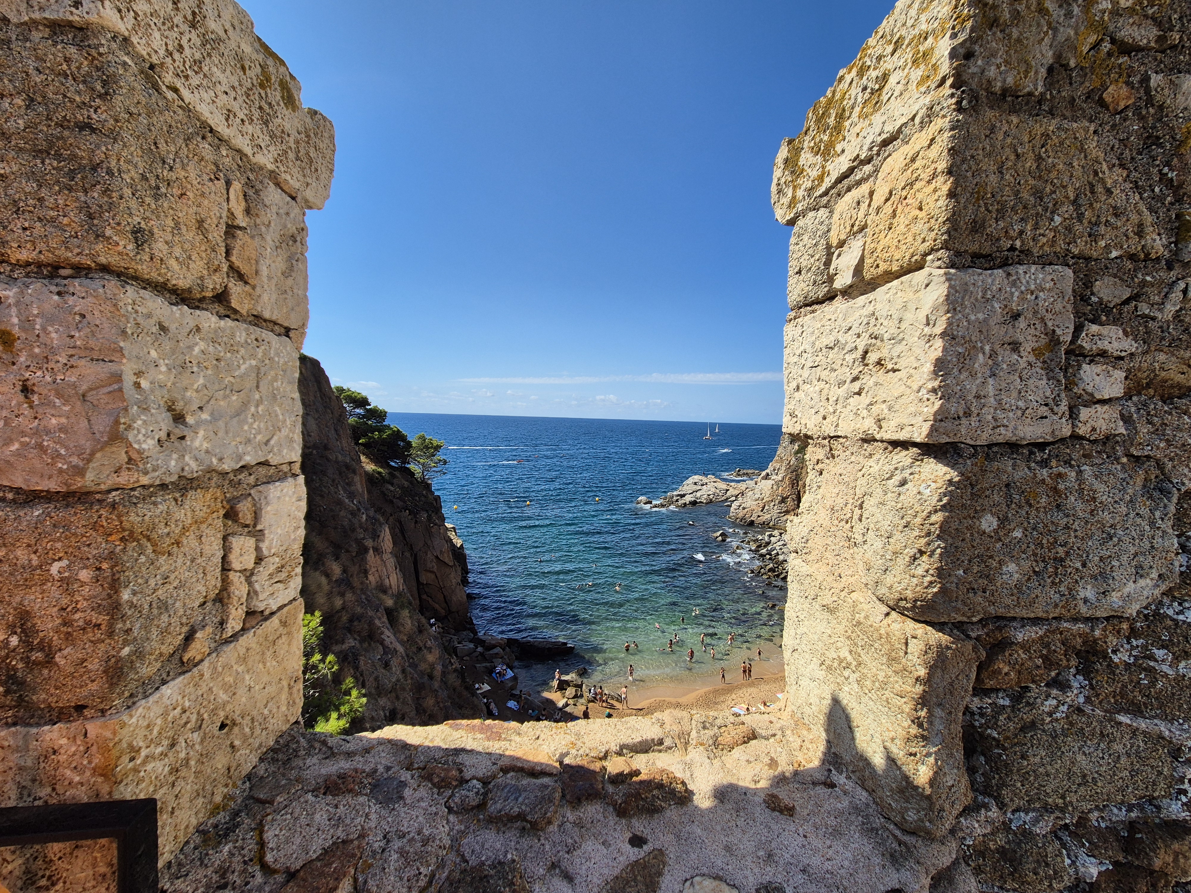 Vista del mar i la platja a través de dues parets de pedra d’una fortificació