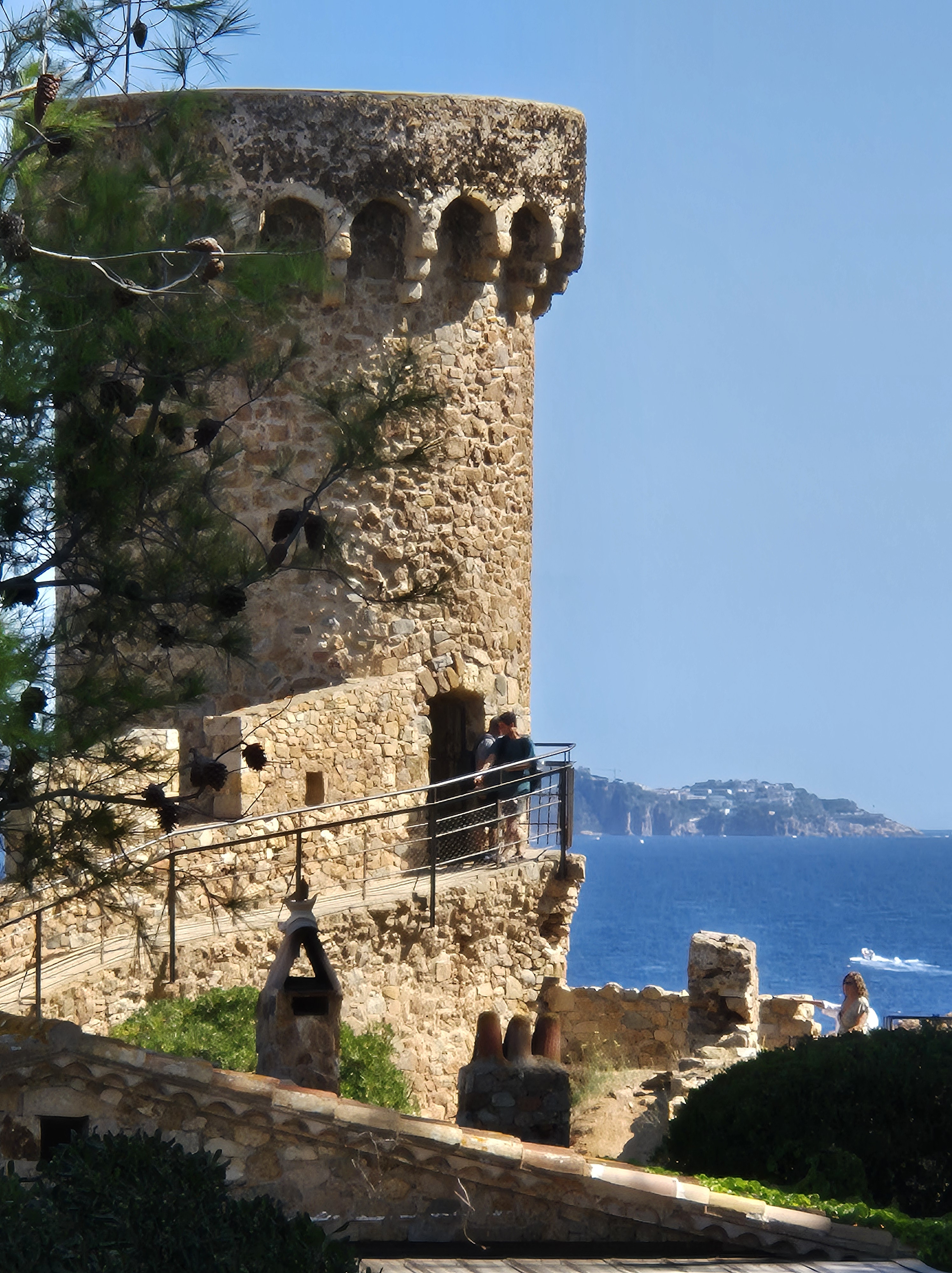 Torre de pedra medieval sobre penya-segat amb vistes al mar, amb camí i barana